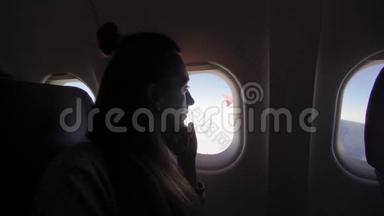 飞机舷窗上的女孩。 年轻女子坐在乘客座位上，在飞机上<strong>看着窗外</strong>。