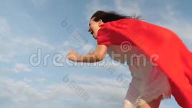 滑稽的超级<strong>英雄</strong>女孩穿着红色斗篷跑着笑，斗篷在风中飘扬。 开朗的年轻女人扮演超级<strong>英雄</strong>