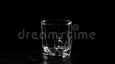 豪华威士忌。 手把金色的威士忌从一个方形的瓶子里倒入旋转的黑色桌子上的玻璃杯里。 不倒翁威士忌。