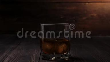 豪华<strong>威士忌</strong>。 冰块落在一杯金色<strong>威士忌</strong>中，放在木制桌子上，背景是木制的。 不倒翁<strong>威士忌</strong>。