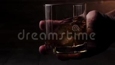 豪华威士忌。 人慢慢地在杯子里用冰块在木制背景下搅拌金色威士忌。 不倒翁威士忌。 波旁酒。