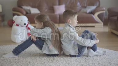 双胞胎男孩和女孩坐在客厅的地板上，背对着对方生气。 兄妹关系