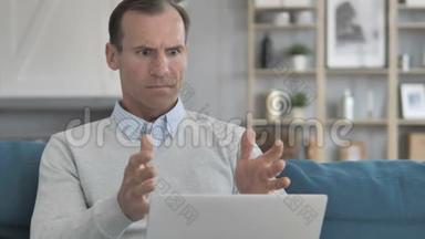 沮丧的老人在坐在沙发上用笔记本电脑面对损失