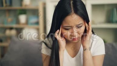 不高兴的亚洲女学生感<strong>到头</strong>痛，并试图释放疼痛，按摩她的头，触摸。