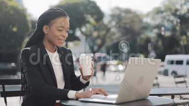 微笑的非裔美国女商人坐在<strong>夏日</strong>露台的<strong>咖啡</strong>馆里，喝着<strong>咖啡</strong>，在笔记本电脑上工作