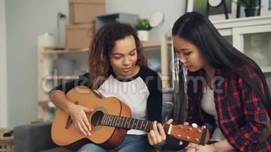 微笑的非裔美国女孩正在教她的亚洲朋友弹声吉他，然后给她的音乐剧