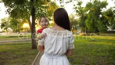 小女儿在妈妈手里，幸福的一家人走在夏日公园里.. 慢动作