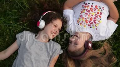 两个戴着耳机的可爱女孩躺在公园里。 美丽的孩子上学时代正在一起度过快乐的时光。