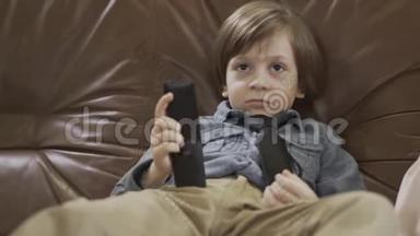 肖像<strong>可</strong>爱的小男孩坐在皮革沙发上，双腿分开，用遥控器在电视上<strong>更换</strong>频道。 <strong>可</strong>爱的儿童