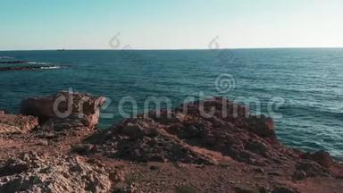 蓝色的海水和棕色的岩石悬崖，地平线上有太阳。 塞浦路斯的珊瑚海滩。 蓝色海水碰撞的鸟瞰图