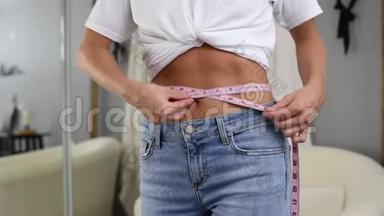 穿牛仔裤站在镜子前的幸福女人正在测量<strong>减肥</strong>后的腰围