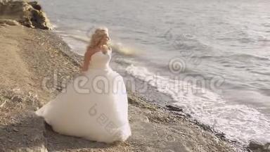 美丽可爱的新娘在海边漫步.. 漂亮又整洁的女人。 金发。 天气晴朗。 婚礼