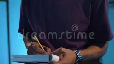 穿紫色t恤的男人坐在有蓝色墙壁的房间里，在笔记本上写笔记