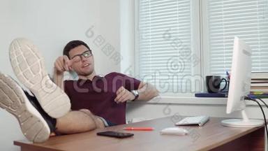 年轻懒惰的办公室工作人员戴着眼镜在办公室里放松，双腿放在桌子上，在现代办公室里扔碎片
