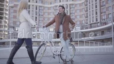 穿着棕色外套和浅<strong>蓝色</strong>牛仔裤的英俊严肃的男子，骑着自行车站在城市的<strong>高楼</strong>前