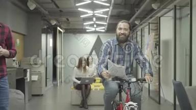 有胡子的微笑积极的男人骑着自行车，手里拿着<strong>文件</strong>，向办公室里的女士<strong>展示文件</strong>