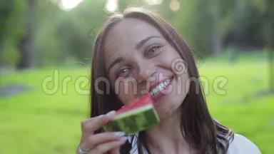 特写女孩的肖像，闻着香气，吃着一个红色的健康多汁的西瓜，在绿色的西瓜上傻笑