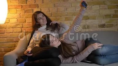 年轻的高加索女孩在沙发上放松，在舒适的家庭氛围中使用智能手机制作自拍照片的肖像。