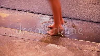 一个孩子赤脚站在车道底部的<strong>水</strong>坑里。 他们动作缓慢，<strong>溅起水</strong>花降落