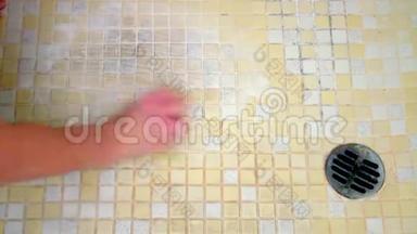 一个女人的手开始用海绵清洁由黄色和白色瓷砖组成的肮脏的淋浴地板