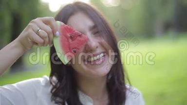 特写女孩的肖像，闻着香气，吃着一个红色的健康多汁的西瓜，在绿色的西瓜上傻笑