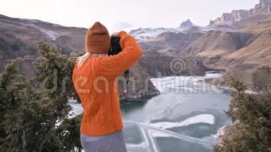 后景女孩摄影师<strong>旅行</strong>者穿着橙色毛衣和帽子，在他的dslr相机景观上<strong>拍照</strong>。