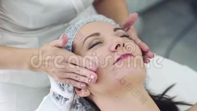 美容院美容师的双手合拢，用闭着眼睛给女人做面部按摩。