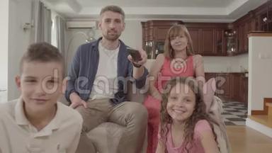 描绘了快乐的年轻家庭一起坐在家里看电视。 父亲<strong>拿</strong>着<strong>遥控</strong>器开关