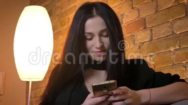 年轻的黑发白种人女孩在智能手机手表上打字的肖像，在家庭氛围中微笑成相机。