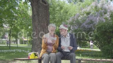 肖像可爱的成年夫妇看着<strong>老照片</strong>，回忆着坐在公园长凳上的快乐时刻。 成熟的夫妻