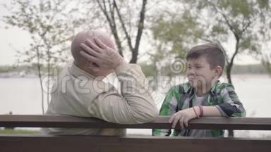 爷爷和孙子坐在<strong>河边</strong>的<strong>公园</strong>里的长凳上，老人给男孩讲了一个有趣的故事