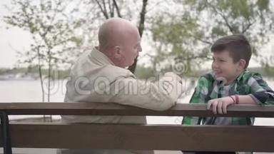 爷爷和孙子坐在河边的公园里的长凳上，老人给男孩讲了一个有趣的故事
