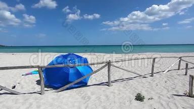 被遗弃的白色海滩，带着一把蓝色的海滩伞，从后面看到，在蓝色的大海和蓝色的背景下，在风中飘扬