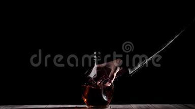 豪华白兰地。 穿黑色衬衫的人把一个圆形的瓶子放在木桌上，背景是黑色的。 白兰地，白兰地，嗅探器。