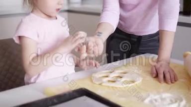 一位母亲和她金发的女儿在厨房准备<strong>饼干</strong>。 小女孩用金属形状<strong>切</strong>割<strong>饼干</strong>