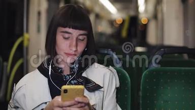 年轻时尚的女士戴着耳机听音乐，在<strong>公共交通工具</strong>上浏览手机。 城市