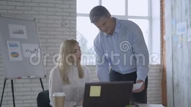 男人和女人的同事正在使用笔记本电脑聊天，分享现代办公室的商业想法。 女孩坐在书桌前