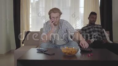 一个英俊的长胡子<strong>男人</strong>坐在沙发上用手机说话，而他的非裔美国人朋友正看着他的<strong>背影</strong>