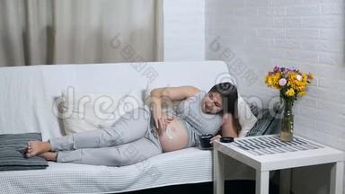幸福的孕妇躺在家里的沙发上，用面霜涂抹在肚子上，<strong>露出笑容</strong>