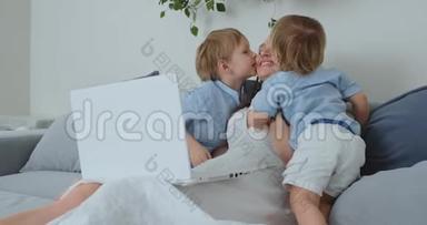 妈妈坐在沙发上拿着笔记本电脑。 两个男孩的<strong>孩子唱歌</strong>，亲吻他们的母亲。 家庭幸福，充满爱心