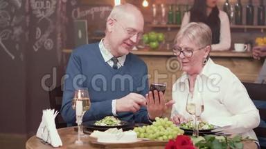 一对漂亮的老夫妇在老式餐厅约会，看着智能手机上的照片