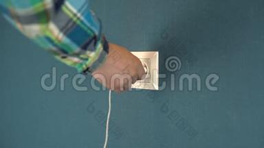 一个男人把电话充电器插入墙上的插座。 墙上贴着深蓝色壁纸的罗塞特