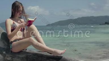 塞舌尔。 普拉斯林岛。 这位年轻貌美的女士坐在树干上看书，在水上看书