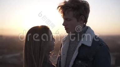 年轻的金发男孩和她的长发女朋友站在罗格在日出拥抱。 好好享受