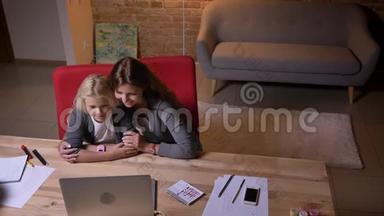 特写镜头，年轻的白种人母亲和她的女儿在笔记本电脑<strong>上</strong>看电影，笑。 妈妈<strong>轻轻地</strong>