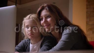 年轻的白种人母亲和她漂亮的小女儿拥抱在一起看电影的特写镜头