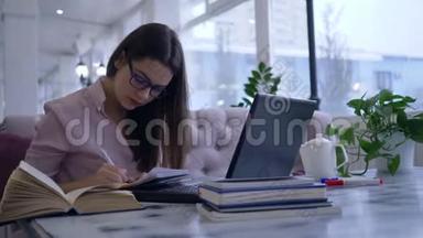在线课程，学生女孩在笔记本上写笔记，看书坐在桌上用笔记本电脑