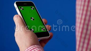男人`手拿着智能手机在一个垂直的位置，并作出触摸手势。 手机上的绿色屏幕和蓝色