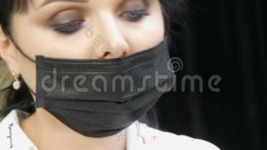戴黑色面具的美容师做这个手术。 一位戴医用口罩的年轻美女的特写