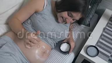 幸福的孕妇躺在家里的沙发上，用面霜涂抹在肚子上，<strong>露出笑容</strong>